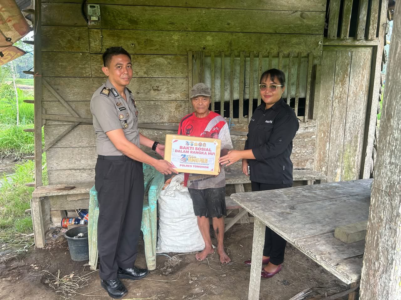 Personel Humas Polres Tomohon menyerahkan paket sembako bakti sosial HUT ke-75 Humas Polri kepada warga